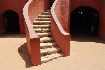 Vue d'un détail de l'escalier de couleur orangée de la maison des esclaves de l'île de Gorée au Sénégal. Rampe de forme incurvée. Architecture coloniale. Bâtiment rénové et coloré. Avril 2024.