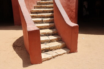 Vue d'un détail de l'escalier de couleur orangée de la maison des esclaves de l'île de Gorée au Sénégal. Rampe de forme incurvée. Architecture coloniale. Bâtiment rénové et coloré. Avril 2024.