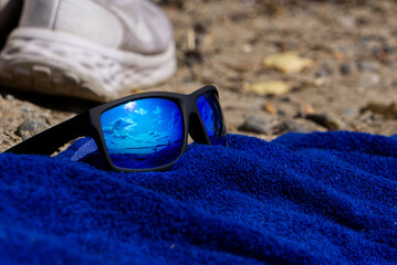 blue reflection in sunglasses by the beach on a lue towel