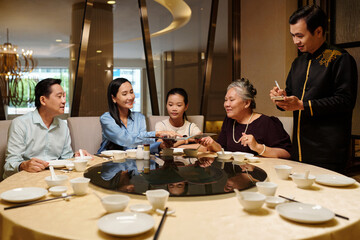 Waiter taking order from family while they sitting at dining table