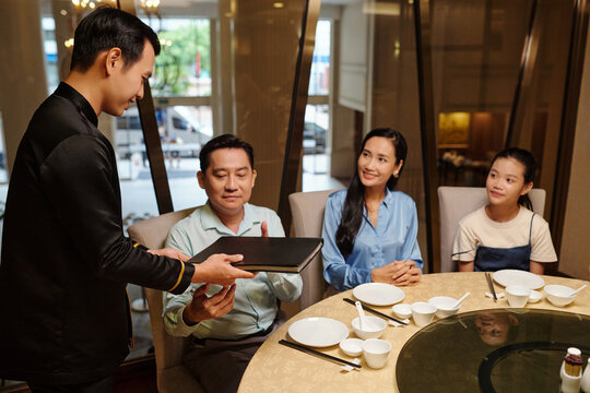 Waiter giving menu to family to make order in the restaurant