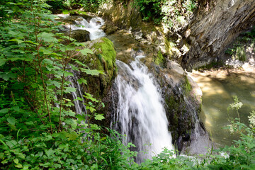 A small waterfall flows into a calm river in the forest. Natural landscape. Long exposure
