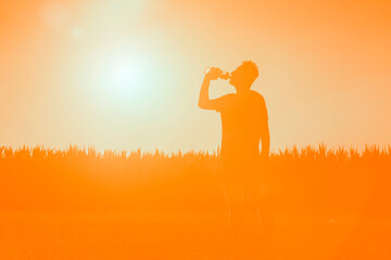 Young man drinks refreshing water while exercising and running. Silhouette of an athlete with a bottle of water on the background of the sun.