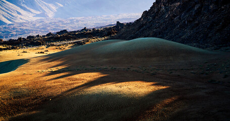 A desert landscape with sandy valleys among mountains and volcanoes at sunset.