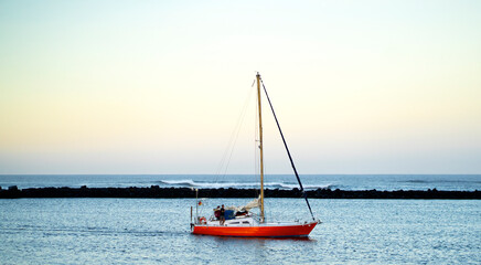 A red yacht sails across the Atlantic Ocean at sunset.