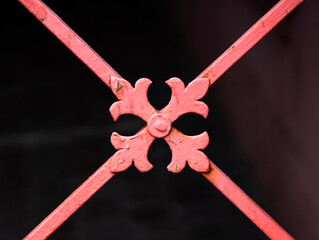 A detail of a forged metal gate in a red color on a dark background.