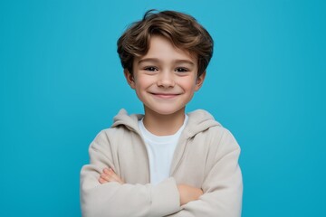Happy kid with arms crossed smiling on blue background, isolated cheerful child portrait