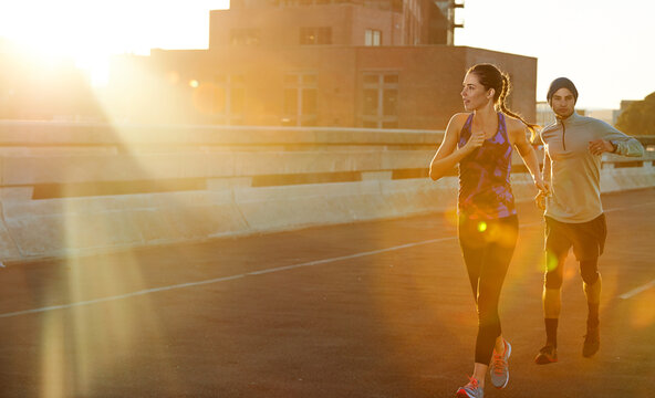 Running, man and woman in city at sunset for fitness, training and commitment to healthy body. Evening, exercise and athlete couple on road for urban workout, outdoor challenge or sports performance