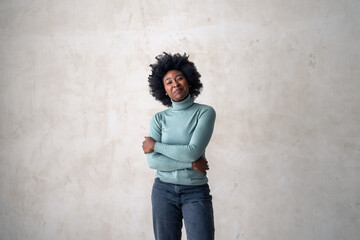 A poised black woman in casual attire stands with her arms crossed. Her expression is relaxed, set against a subtle grey backdrop.