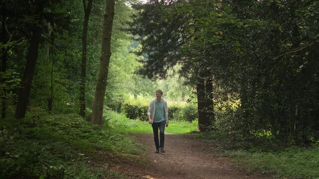 Young man enjoying a relaxed walk in scenic nature. Hiker on a trail in an idyllic forest or park, turning around and taking in the view
