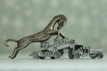 A close-up of a vintage metal horse figurine trampling over antique metal toy cars, creating a...