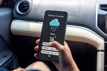 Hand of woman in a car holding a mobile phone to check weather forecast