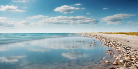 A expansive body of water rests upon a sandy shore under a blue sky, dotted with a few white clouds.