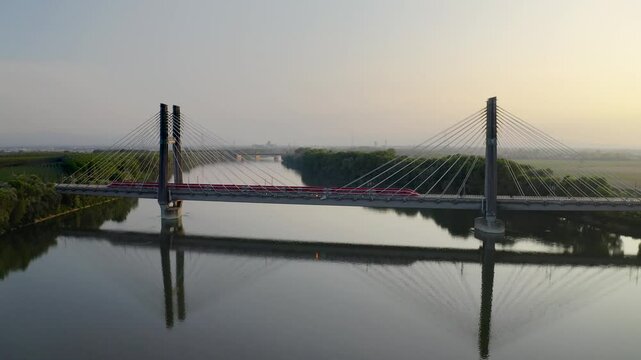 Aerial view of a Frecciarossa train crossing the high-speed rail bridge over the Po River near Piacenza, Italy. The tranquil evening setting reflects the modern marvel of Italian rail engineer