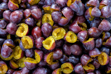 Hand-pitted raw plums. Plums are prepared for jam. Yellow sweet flesh. Close-up of fresh plums, top view. Purple plums background.