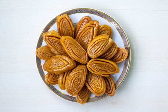 Delicious gaja (also known as khaja, chiroti, or chirote) in a white plate on a light wooden surface. This traditional sweet treat is popular in Bangladesh and the Bengal region of India. Top view.