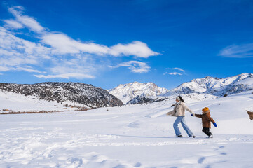 Mom and son running on a snow-covered slope against the backdrop of a mountain landscape in winter.