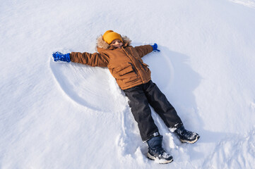 A five-year-old Caucasian boy lies in the snow and makes a snow angel