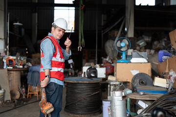 Senior male construction worker using walkie-talkie and woking in warehouse of tower crane assembly factory.