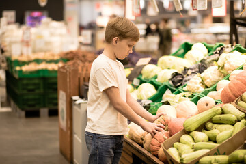 Kid teenager shopping for fresh organic fruits and vegetables in supermarket. Cute boy holding pumpkin in a hands.