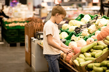 Kid teenager shopping for fresh organic fruits and vegetables in supermarket. Cute boy holding pumpkin in a hands.