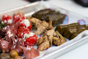 Platter of various Israeli street food pickles, including hibiscus flowers with cheese, dolma, cheeses, olives, and tomatoes with cheese. Rich and diverse flavors of Israeli cuisine.