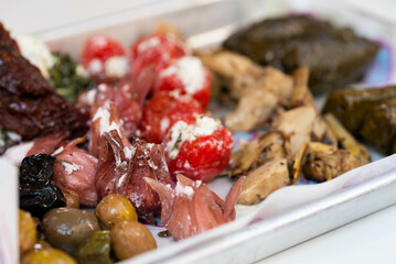 Platter of various Israeli street food pickles, including hibiscus flowers with cheese, dolma, cheeses, olives, and tomatoes with cheese. Rich and diverse flavors of Israeli cuisine.