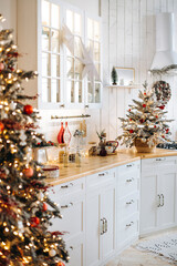 White kitchen with wooden countertops decorated for Christmas. A small Christmas tree with ornaments, a star on the cabinet, and festive accessories create a cozy holiday atmosphere