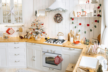 Cozy kitchen decorated for Christmas with white cabinets, wooden countertops, a small frosted Christmas tree with red ornaments, a wreath, garland, and festive touches throughout