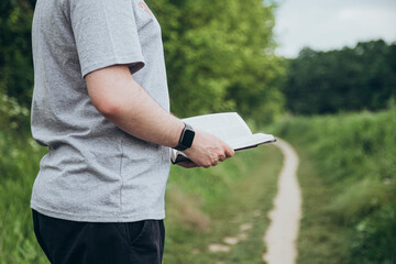 Man is holding the holy Bible outside on a blurred green background.