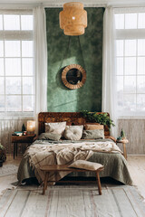 Double bed with wooden headboard placed between two large windows in spacious Christmas-decorated bedroom. Sunlight fills the room, highlighting green walls and festive decor
