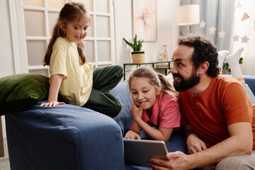 Fototapeta premium Father sitting with daughters while interacting together in living room Family time creating close bond and happy moments together indoors