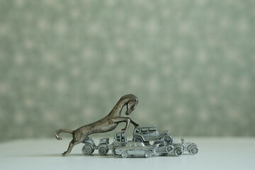 A bronze figurine of a horse trampling antique metal toy cars, creating an image of the power of...