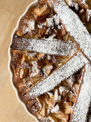 Close-up top view of an open Apple Pie in a round white baking form on a wooden table