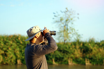 Fototapeta premium Asian man uses binoculars to observe local birds along a river. Soft and selective focus