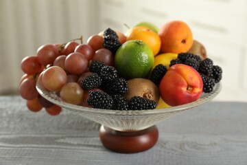 Glass vase with different fruits and berries on grey wooden table indoors, closeup