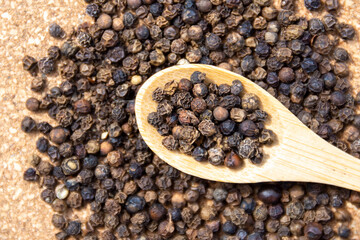Dry black pepper spice on a wooden spoon close up. Black peppercorns.