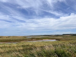 Landscape view of beautiful nature reserve for bird watching wildlife lakes in marsh land by ocean in Cley Next the Sea Norfolk East Anglia uk reeds grass by water lake on Summer day blue cloud skies