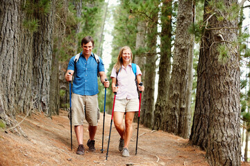 Obraz premium Walking, couple and hiking in forest, smile and adventure for vacation, man and woman with backpack. Outdoor, fun and people with trekking poles, travel and woods with rough terrain in New Zealand