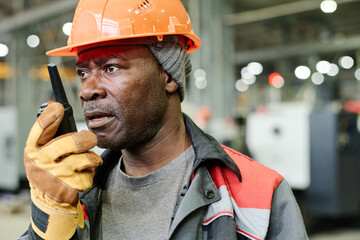 African American worker conversing on walkie talkie in busy construction area wearing protective...