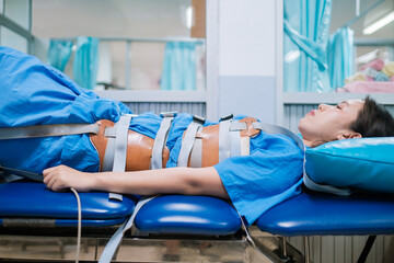 Patient lying on a Mechanical traction physio bed with belt strapped around the body, decompression...
