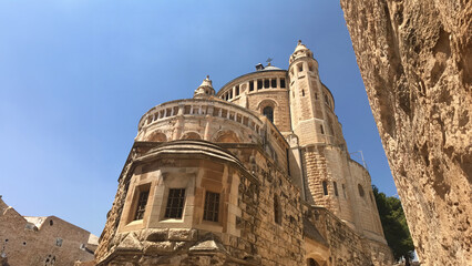 A majestic stone building with intricate architectural details stands tall against a clear blue sky. The angle of the shot emphasizes the grandeur and historic nature of the structure.