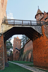 The image captures an ancient castle with red brick walls and a wooden bridge connecting two sections of the fortification.  © Олий Росс