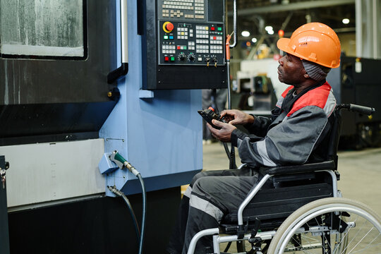 Industrial worker in wheelchair operating complex machinery in manufacturing facility, looking focused and engaged, demonstrating skill and efficiency, emphasizing inclusive work environment