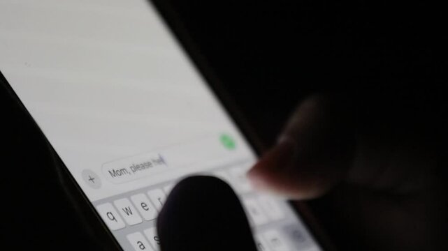 a person typing "mom please help me" on a smartphone in the dark