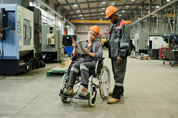 Two factory workers discussing project using tablet in large industrial facility Filled with modern machinery, both displaying collaboration and professionalism
