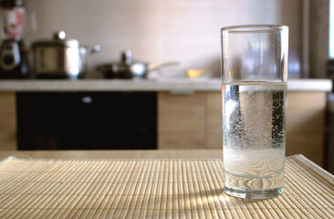 Glass of fresh water on a wooden table in the kitchen. Background with copy space suitable for ads, banners and more. Modern kitchen interior.   