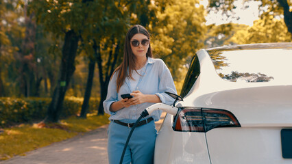 Woman using smartphone online banking application to pay for electric car battery charging from EV...
