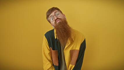 Stylish redhead man with beard wearing glasses over yellow background