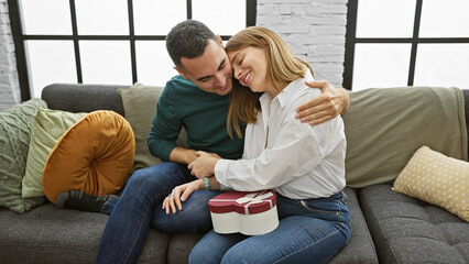 A loving couple embraces on a sofa in a cozy living room, sharing a heartwarming moment with a gift